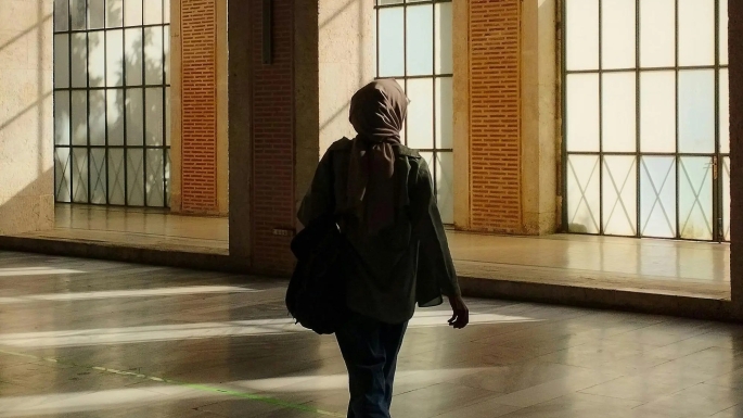 A hijab wearing muslim woman walking through a big empty hallway with large windows